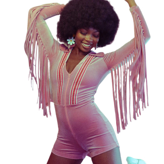 A person wearing a blush pink romper with rainbow stripes and fringe along the sleeves, posing with their arms raised.