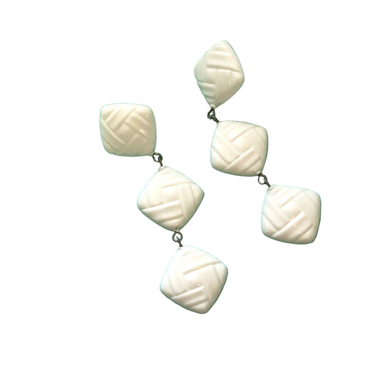 White textured earrings on a green background