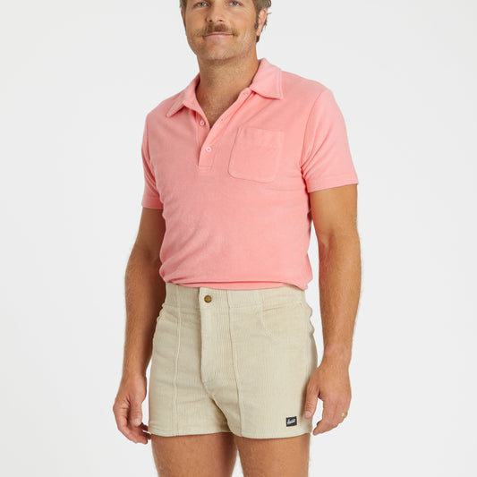 Man wearing a pink polo shirt and beige shorts on a white background